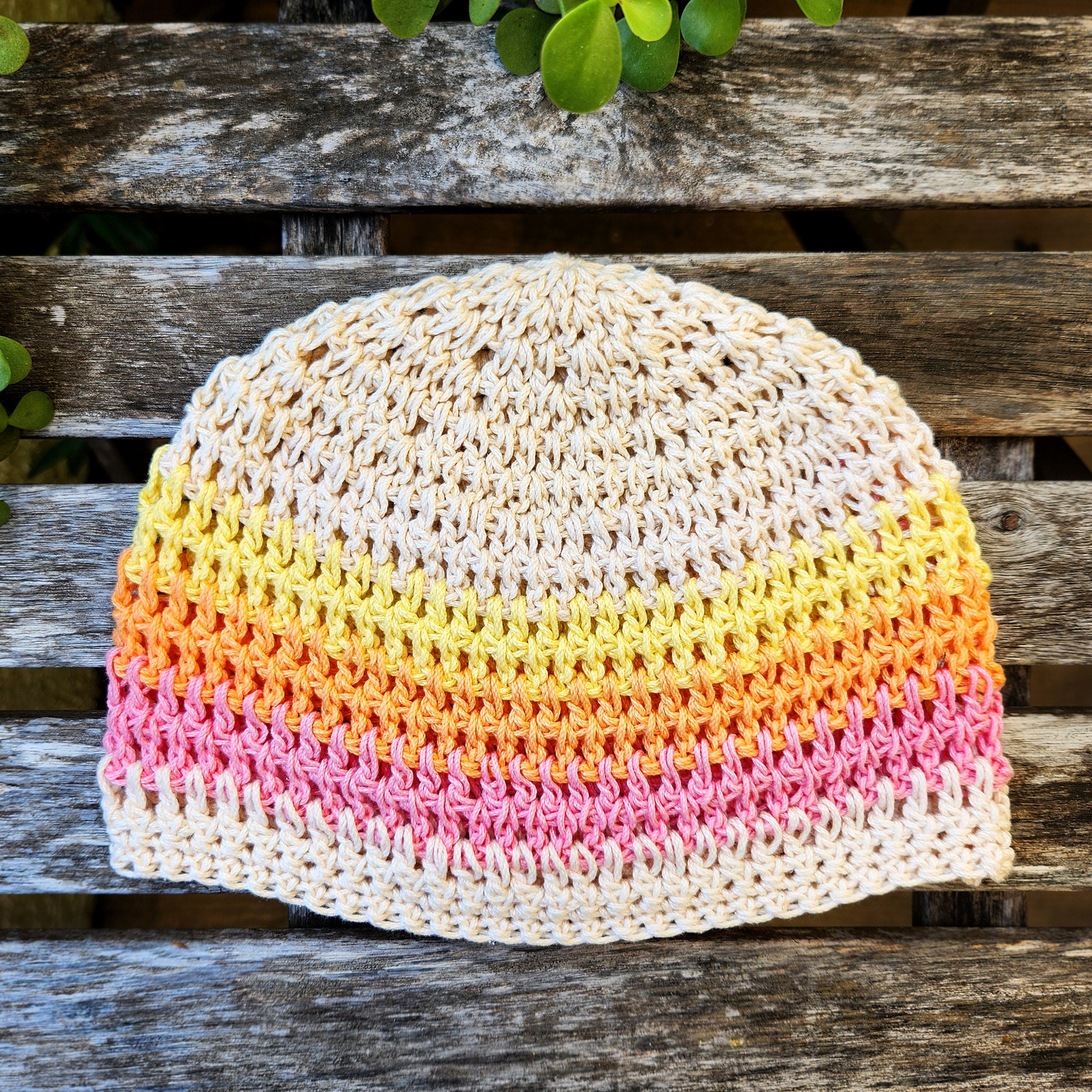 Colorful crocheted beanie on a wooden surface with green leaves.