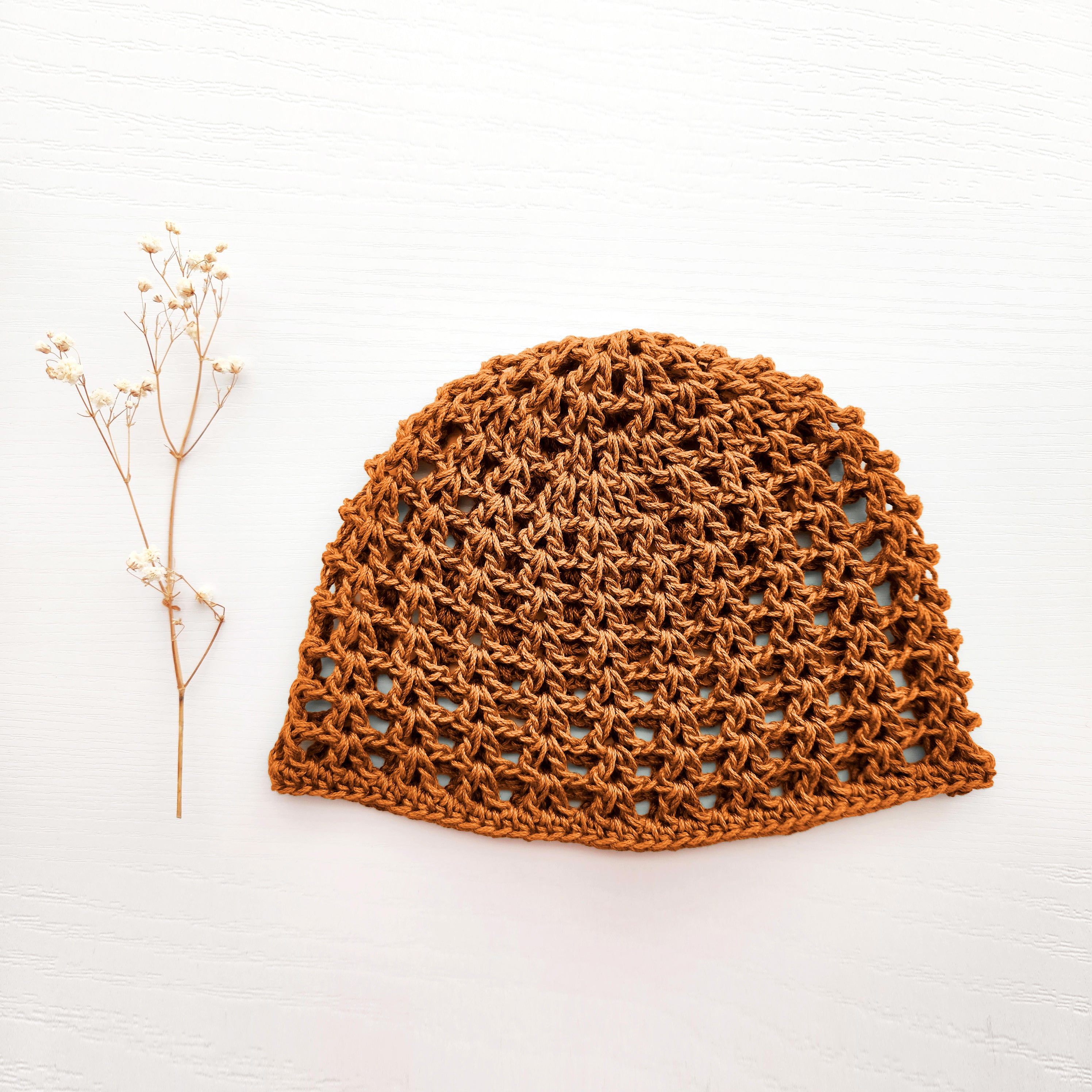 Amber orange crochet hat on a white background with a small branch to the left.