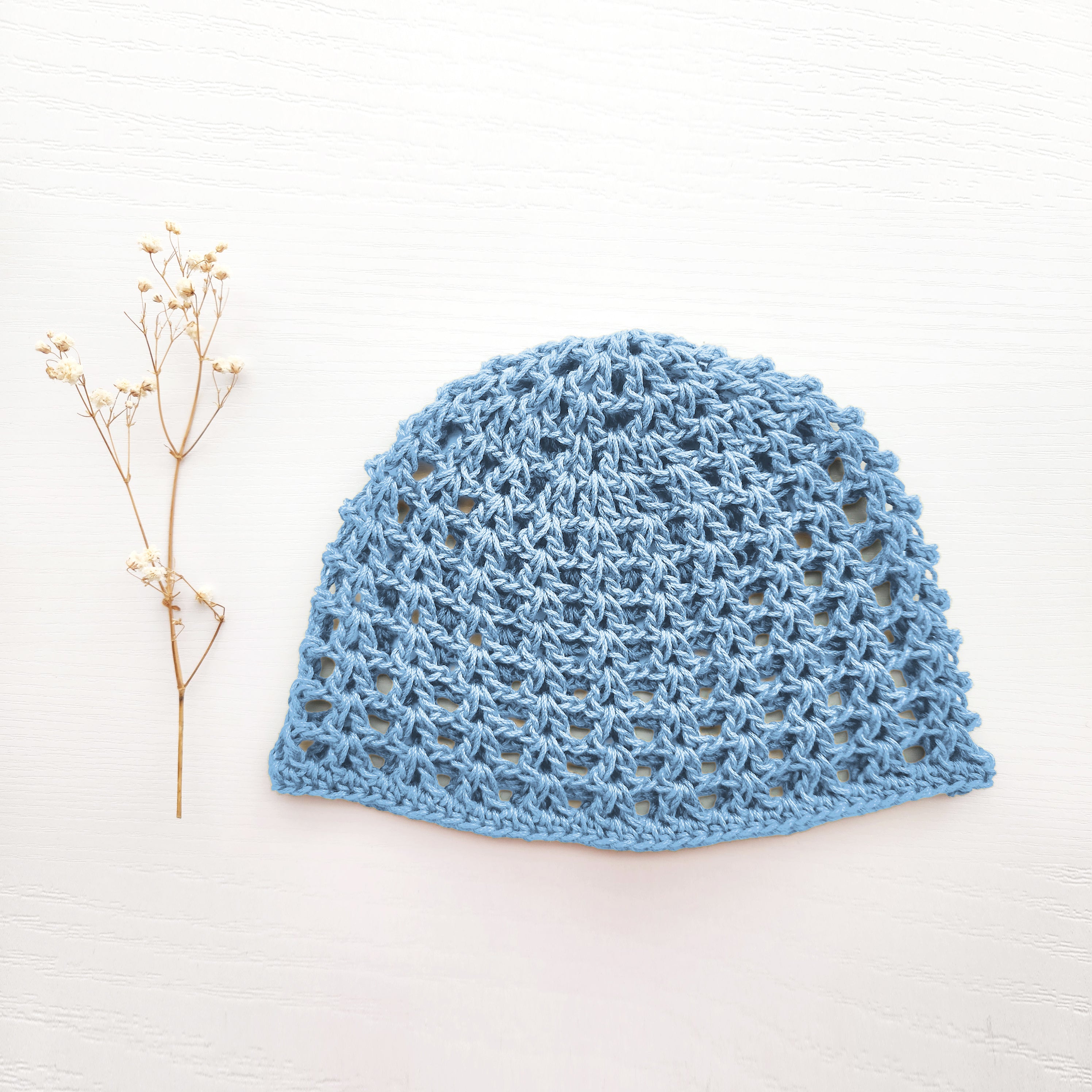 Baby blue crocheted hat on a white background with a small branch to the left.