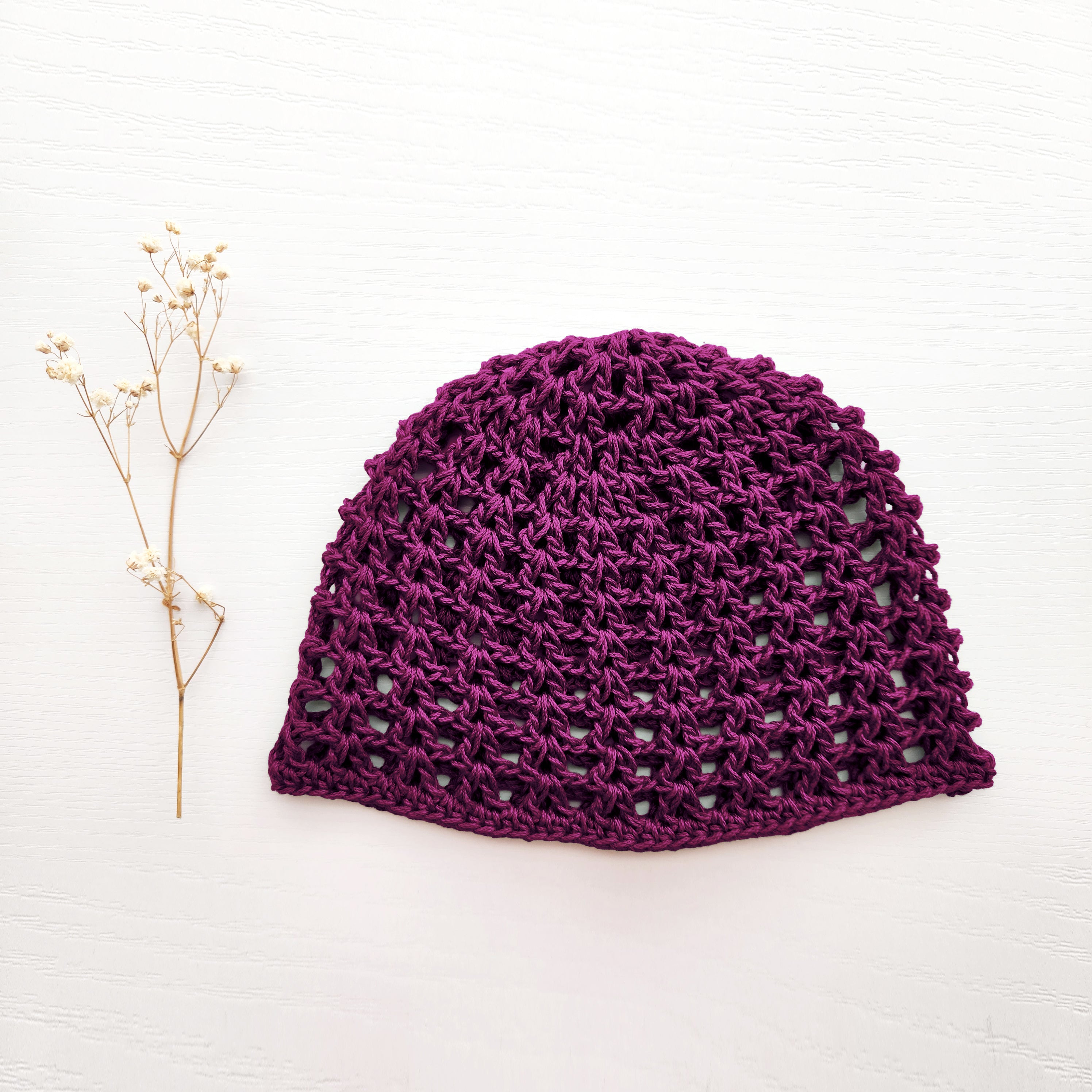 Dark purple knit beanie on a white background with a small branch of flowers.