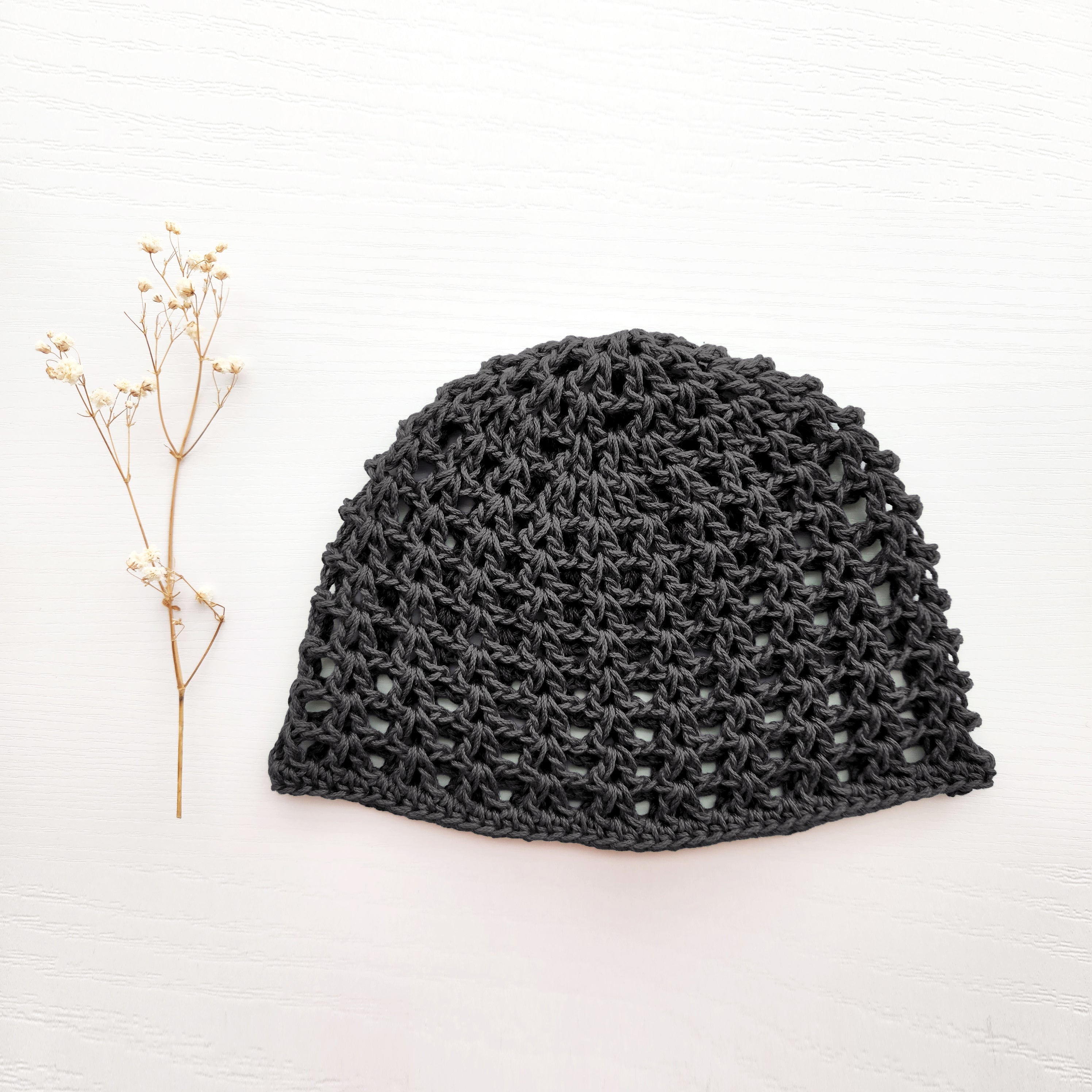 Dark gray knit mesh beanie on a white background with a small branch to the left.
