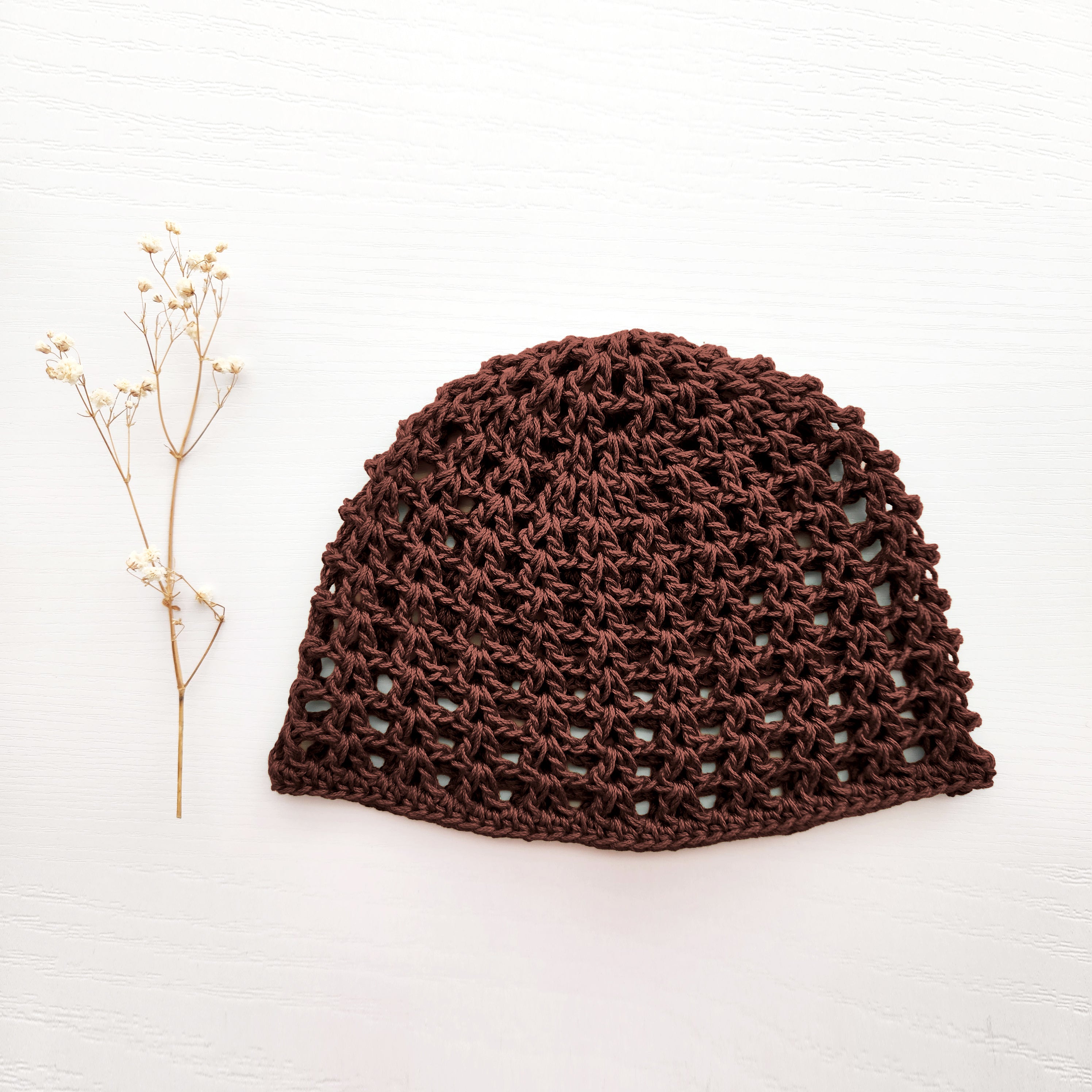 Brown crocheted boho mesh beanie on a white background and a sprig of flowers.