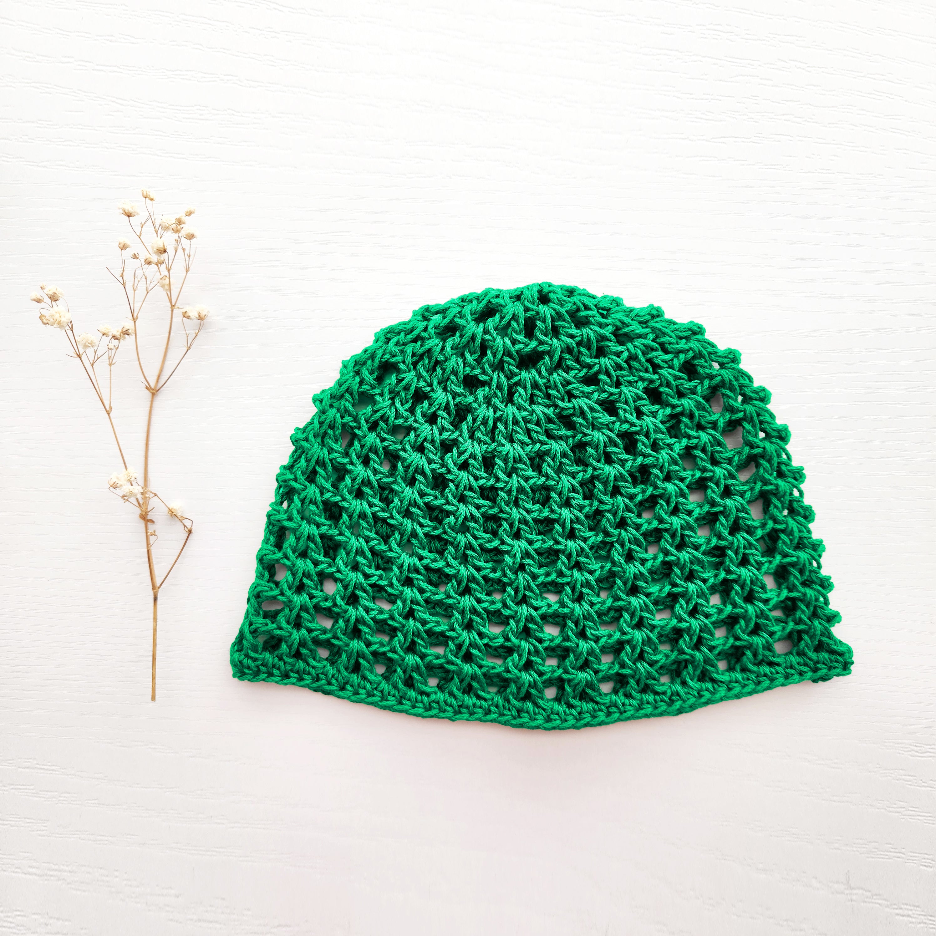 Green knitted hat on a white background with a small branch of flowers.