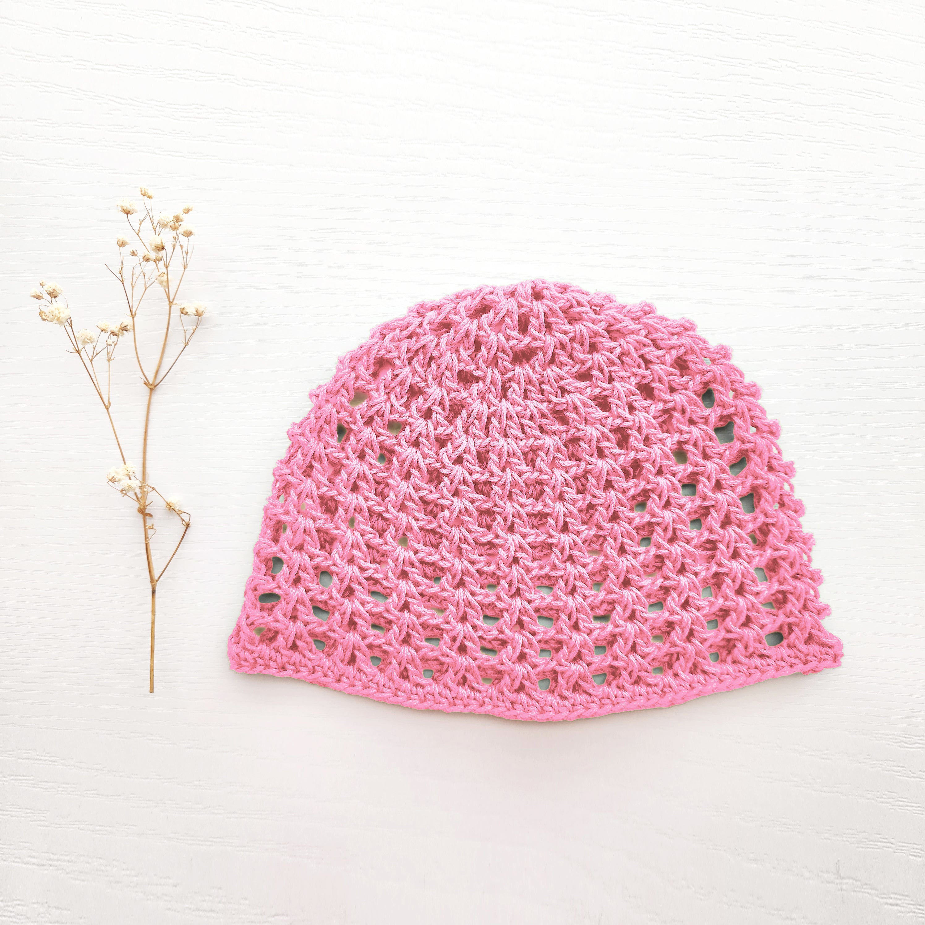Pink crocheted hat on a white background with a small branch to the left.
