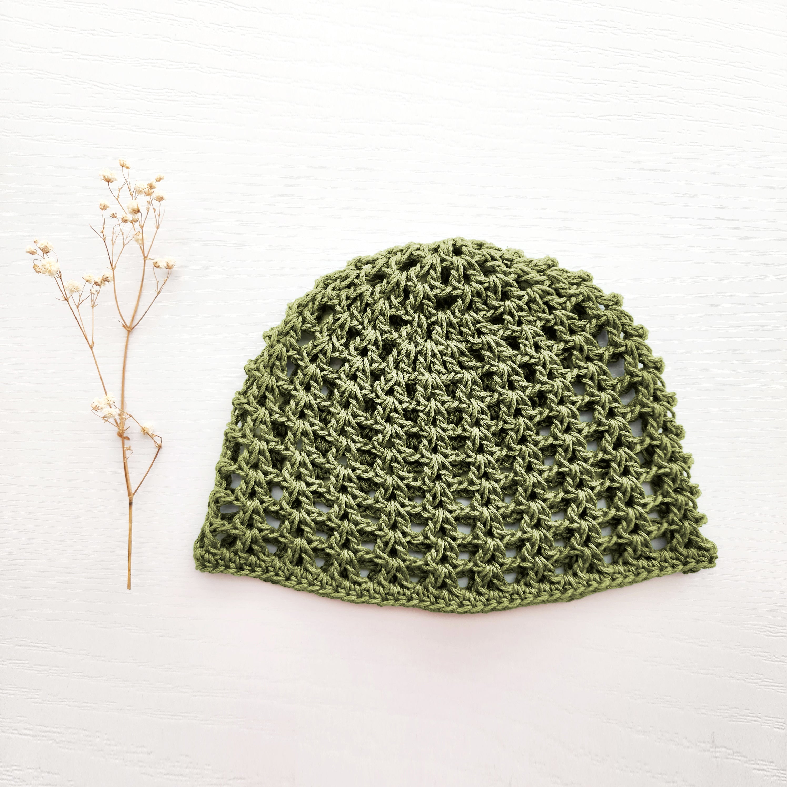 Sage green knitted mesh hat on a white background with a small branch of flowers.