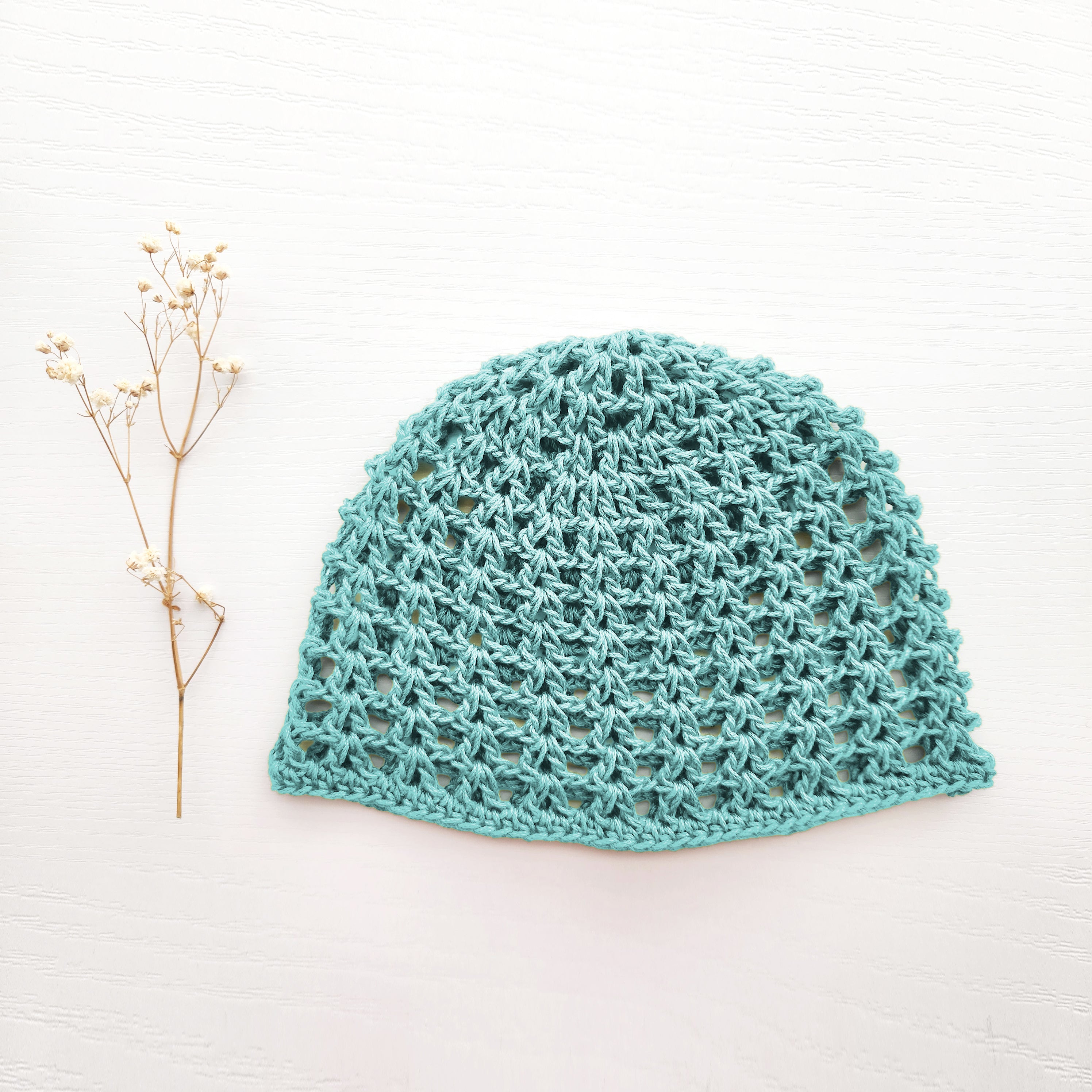 Light sky blue crochet hat on a white background with a small branch to the left.