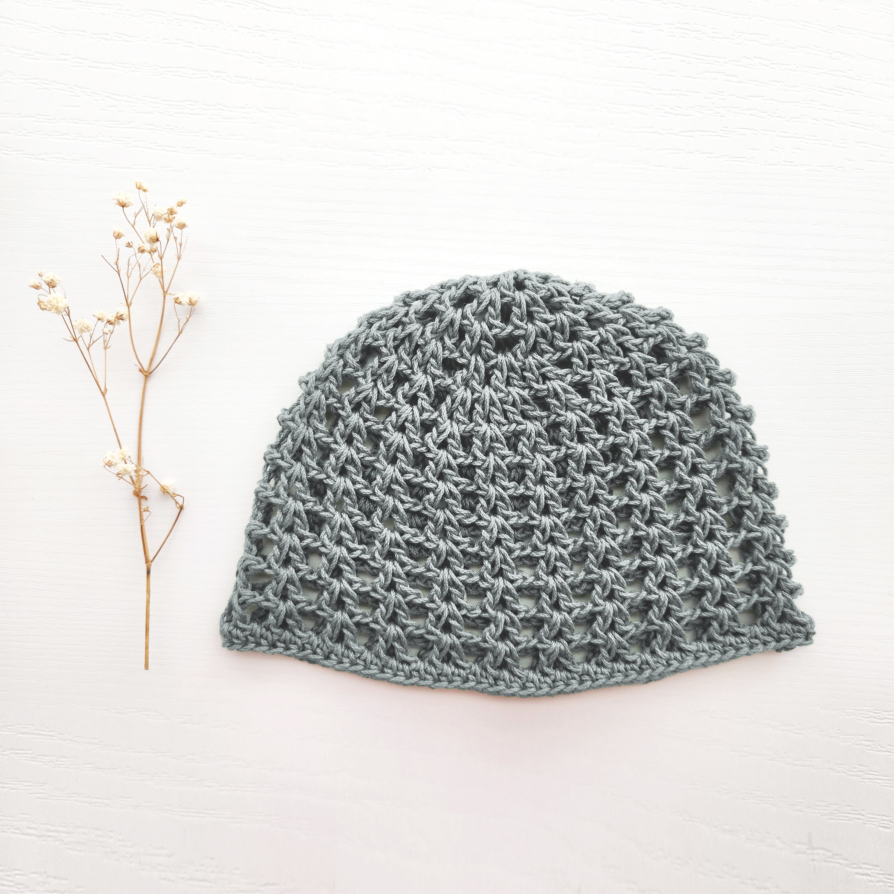 Gray knitted hat on a white background with a small branch to the left.