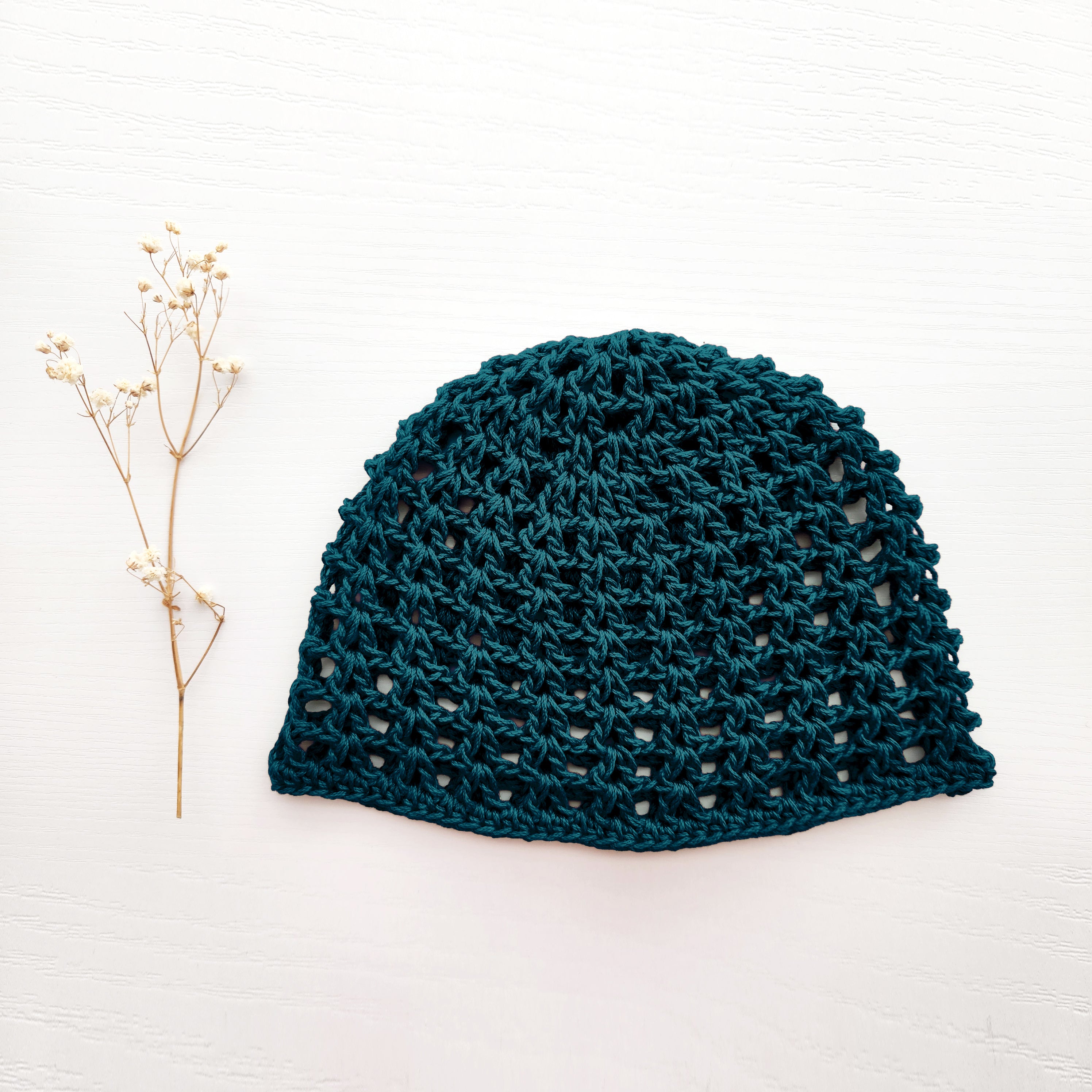 Dark teal knit beanie on a white background with a small branch to the left.