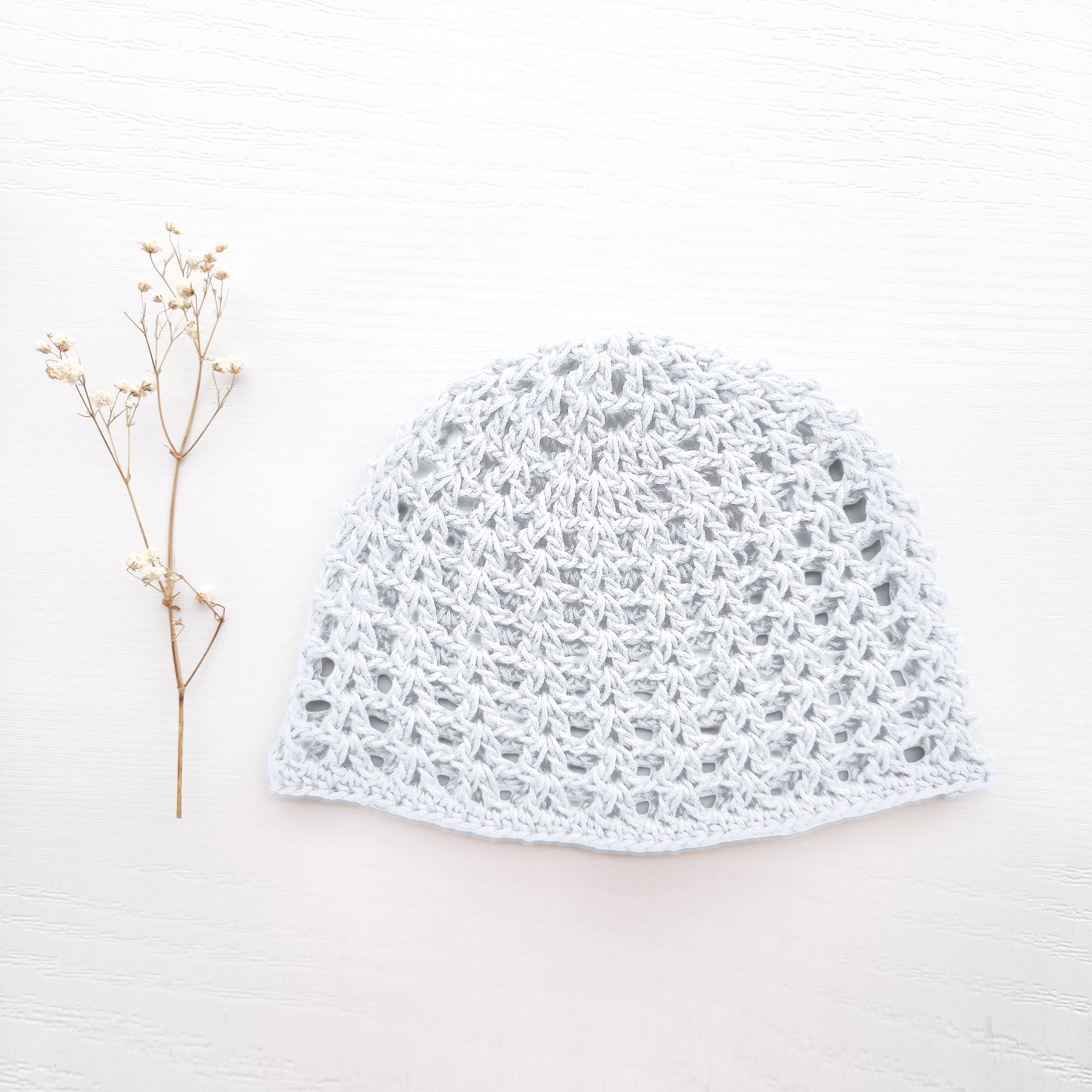White lace crochet hat on a light wooden surface with a small branch.