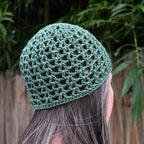 A green knitted beanie worn by a person facing out into a blurred natural background.