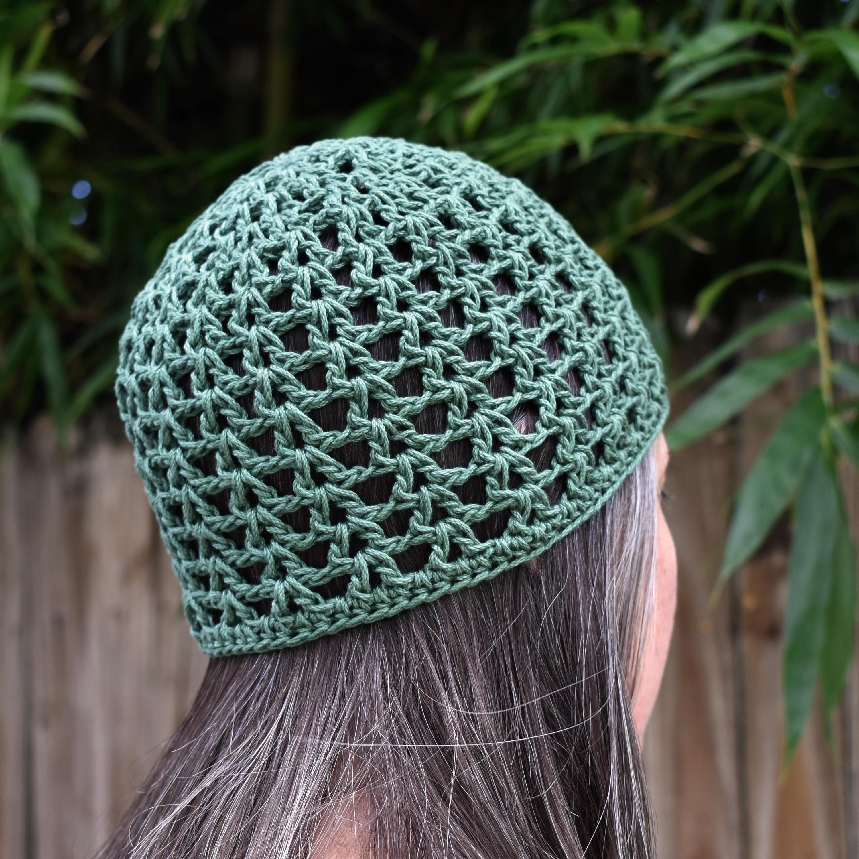 A green knitted beanie worn by a person facing out into a blurred natural background.