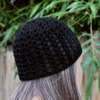 Black knitted beanie worn by a person with gray hair, against a natural background.