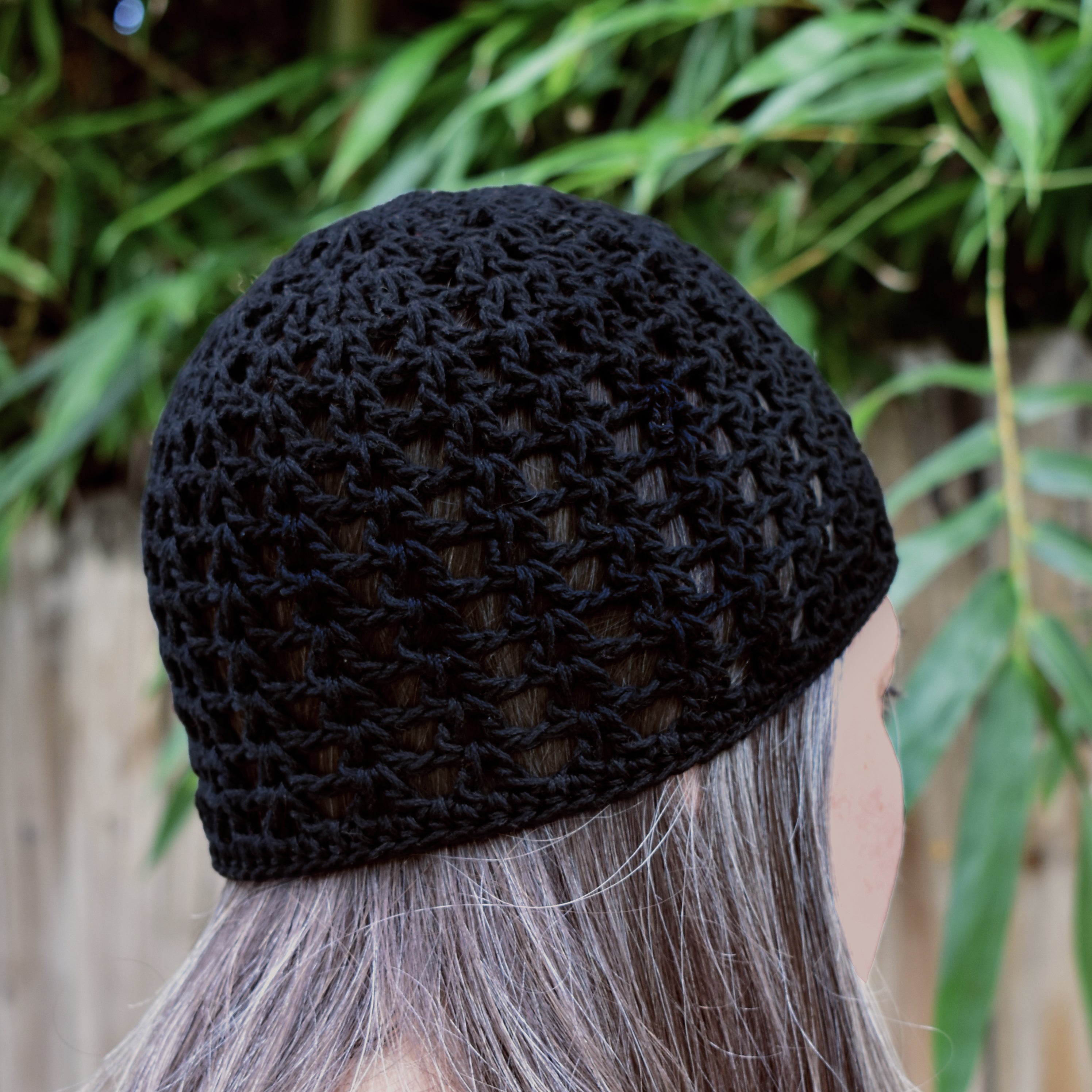 Black knitted beanie worn by a person with gray hair, against a natural background.