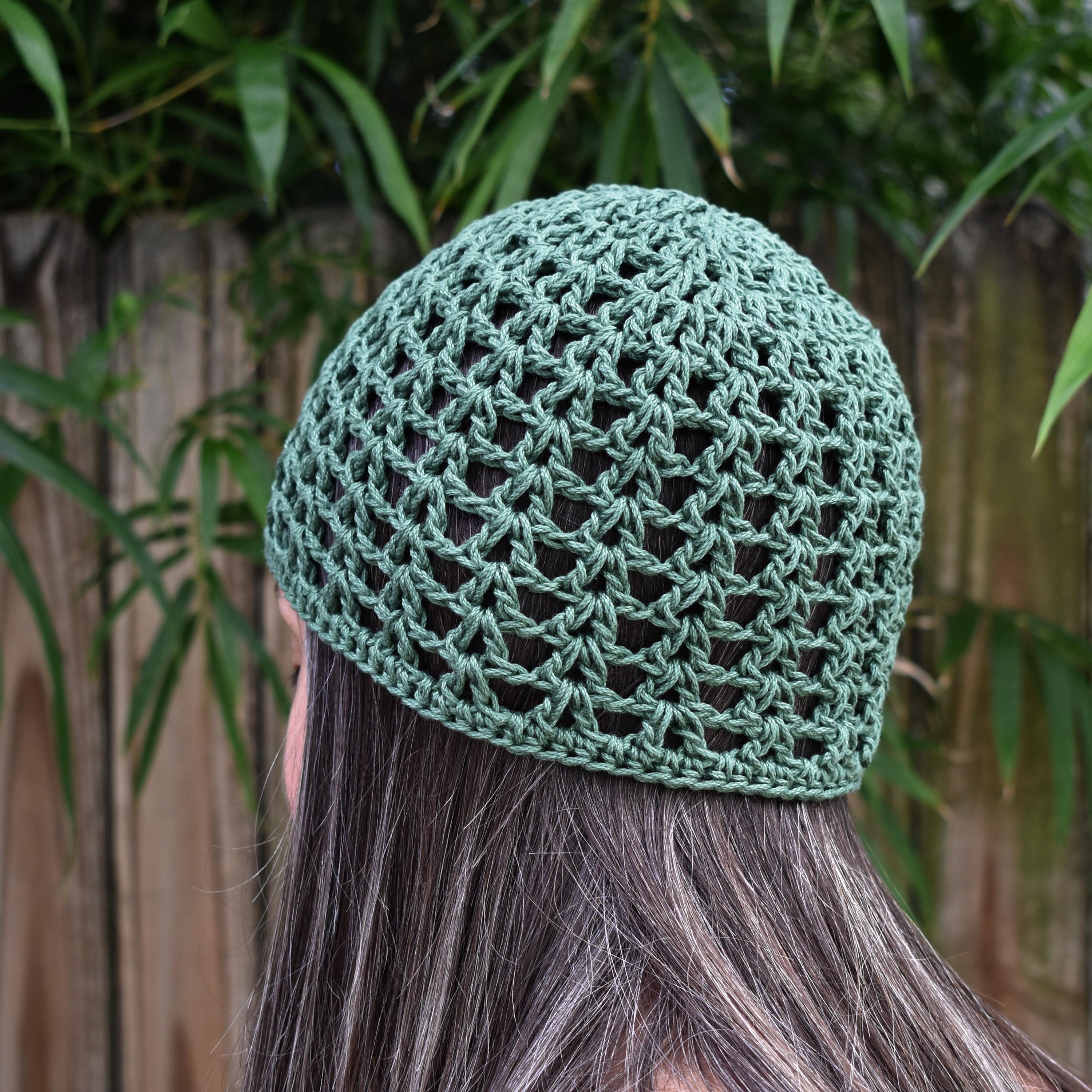 Green knitted beanie worn by a person with a blurred natural background.